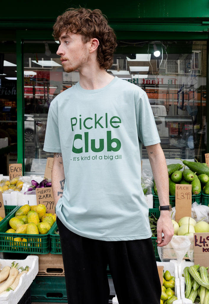model is wearing pickle club tshirt in front of vegetable market