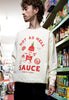 male model is wearing relaxed fit cream sweater with hot sauce logo and vintage style sauce character