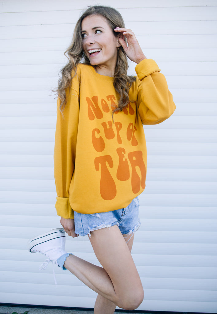 Model wears mustard sweatshirt with Not My Cup of Tea slogan