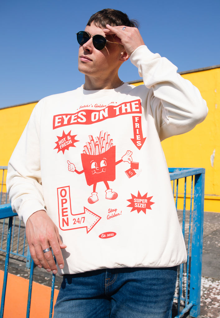 Model wears vanilla sweatshirt with Eyes on the Fries slogan and french fries character graphic