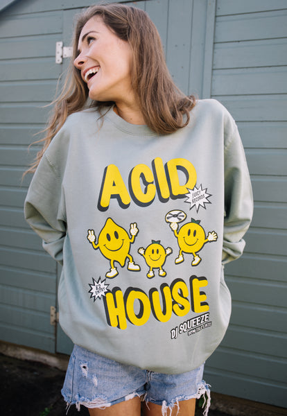 Model wears pastel green sweater with "Acid House" slogan and citrus fruit character graphics