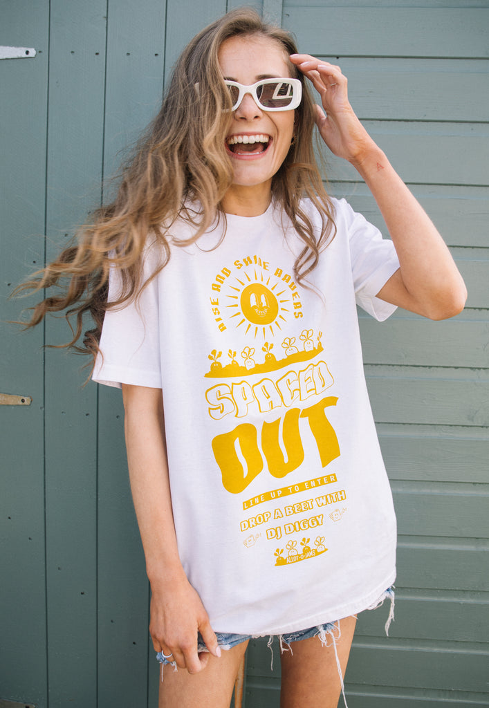 Model wears white t-shirt printed with "Spaced Out" slogan in bright yellow and festival style vegetable graphics