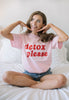 model wears pink cotton relaxed fit crew neck t-shirt with printed detox slogan in red 