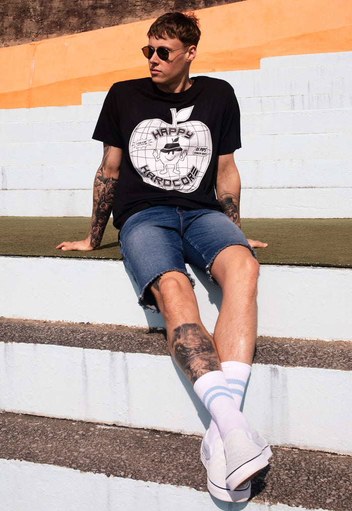 Male model wears black short sleeved t shirt with white printed happy hardcore slogan and apple graphic