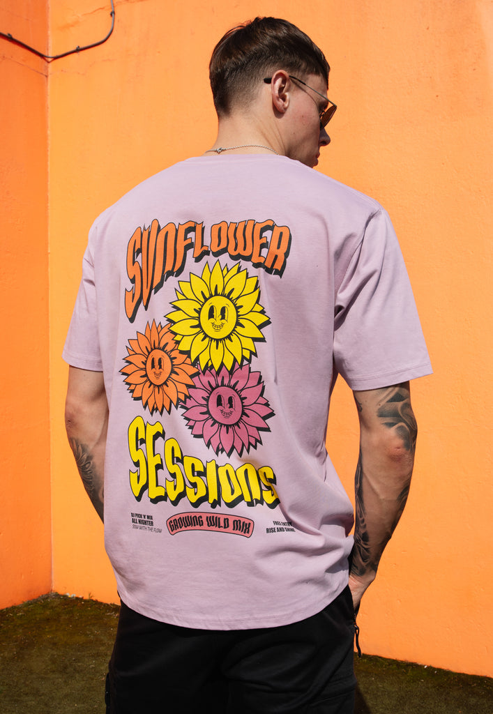 male model wears casual purple t shirt with large back print showing colourful sunflower festival poster graphics