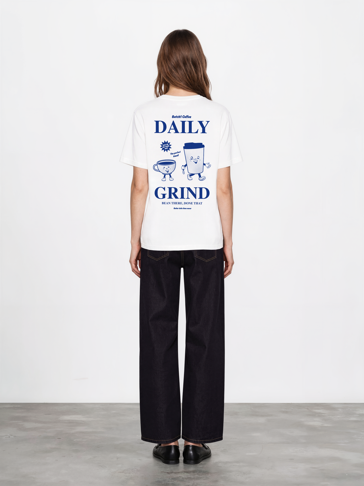 Female model wearing the white Daily Grind T-shirt, back view with dark blue Daily Grind lettering and coffee cup characters.