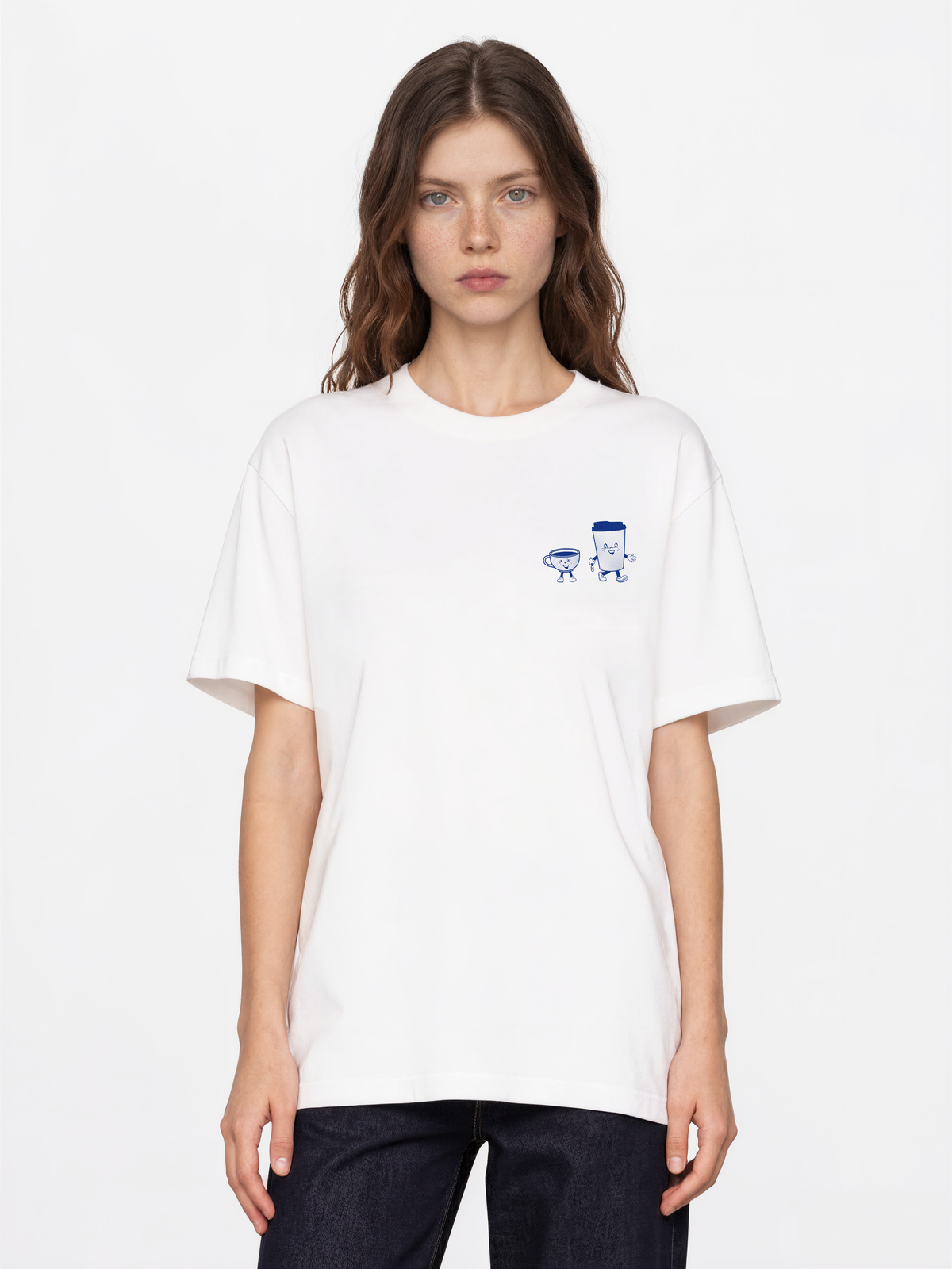 Female model wearing the white Daily Grind T-shirt, front view with dark blue coffee cup characters on the left chest.