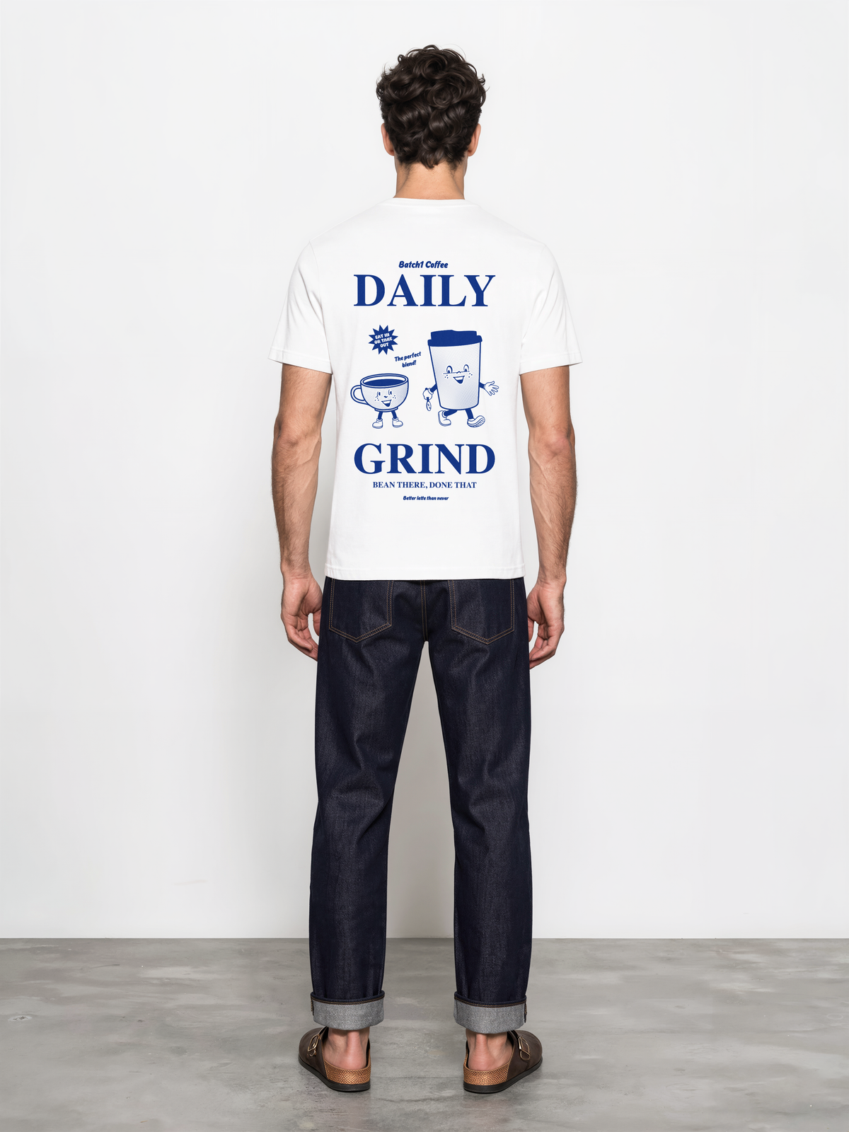 Male model wearing the white Daily Grind T-shirt, back view with dark blue Daily Grind lettering and coffee cup characters.