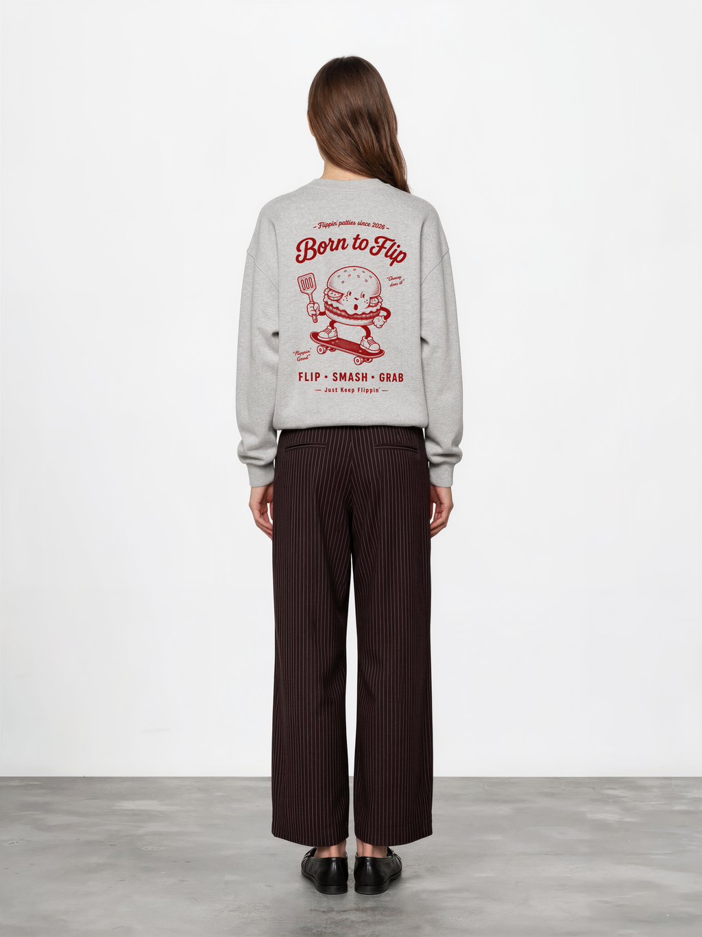 Female model wearing the Born to Flip ash grey oversized sweatshirt, back view with large deep red skateboarding burger artwork across the back.