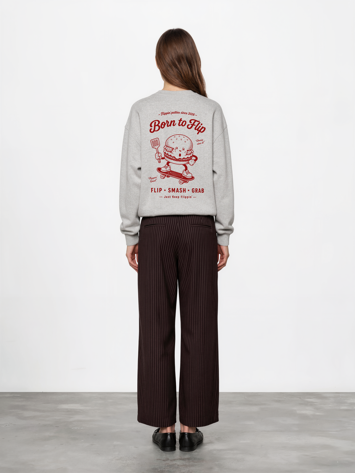 Female model wearing the Born to Flip ash grey oversized sweatshirt, back view with large deep red skateboarding burger artwork across the back.