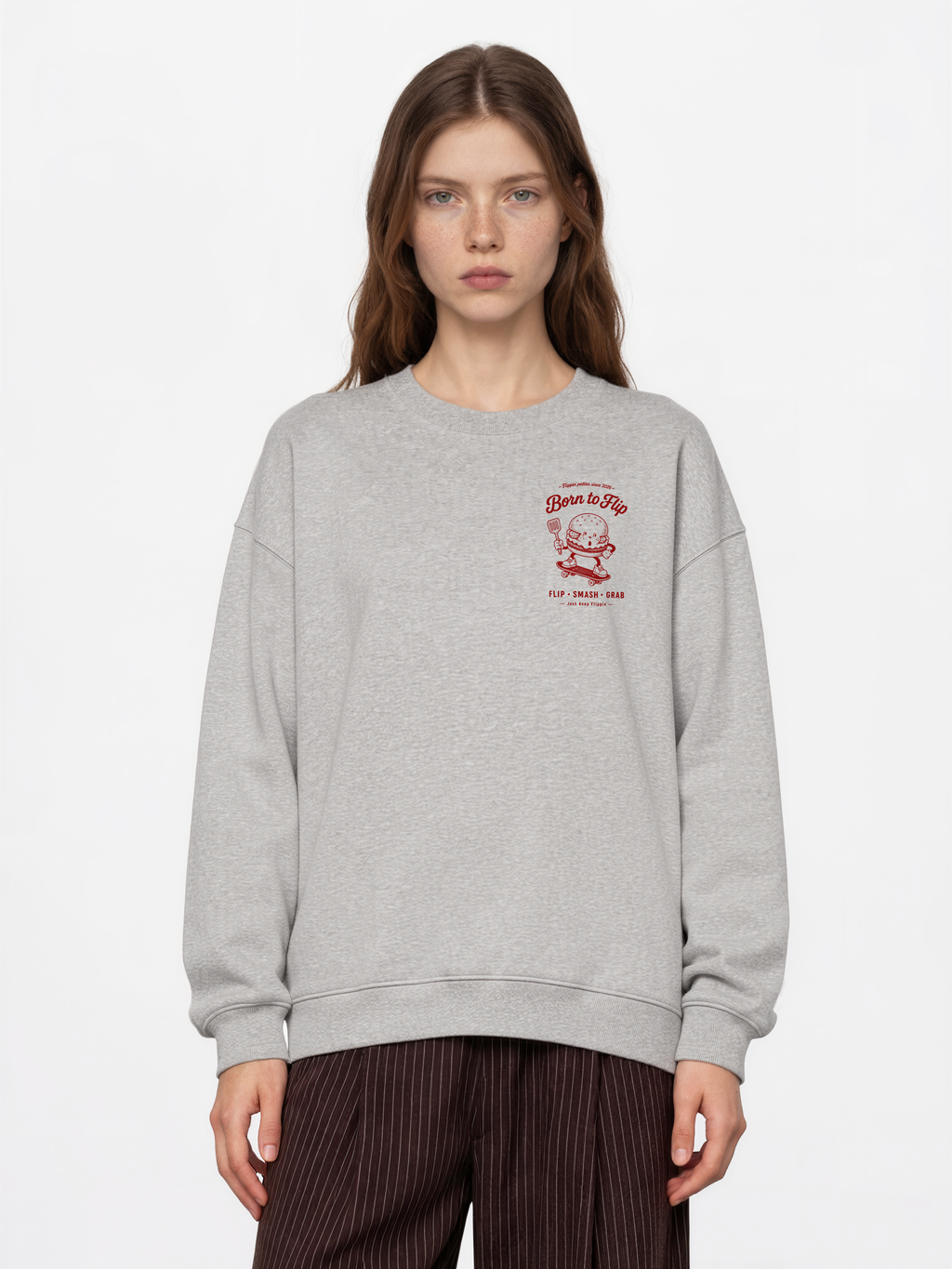Female model wearing the Born to Flip ash grey oversized sweatshirt, front view with small deep red burger artwork on the left chest.