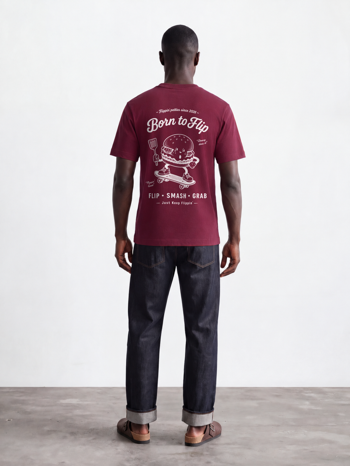 Male model wearing the Born to Flip burgundy T-shirt, back view with large white skateboarding burger artwork across the back.