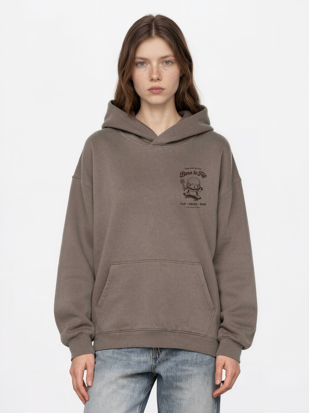 Female model wearing the Born to Flip taupe oversized hoodie, front view with small brown burger artwork on the left chest.