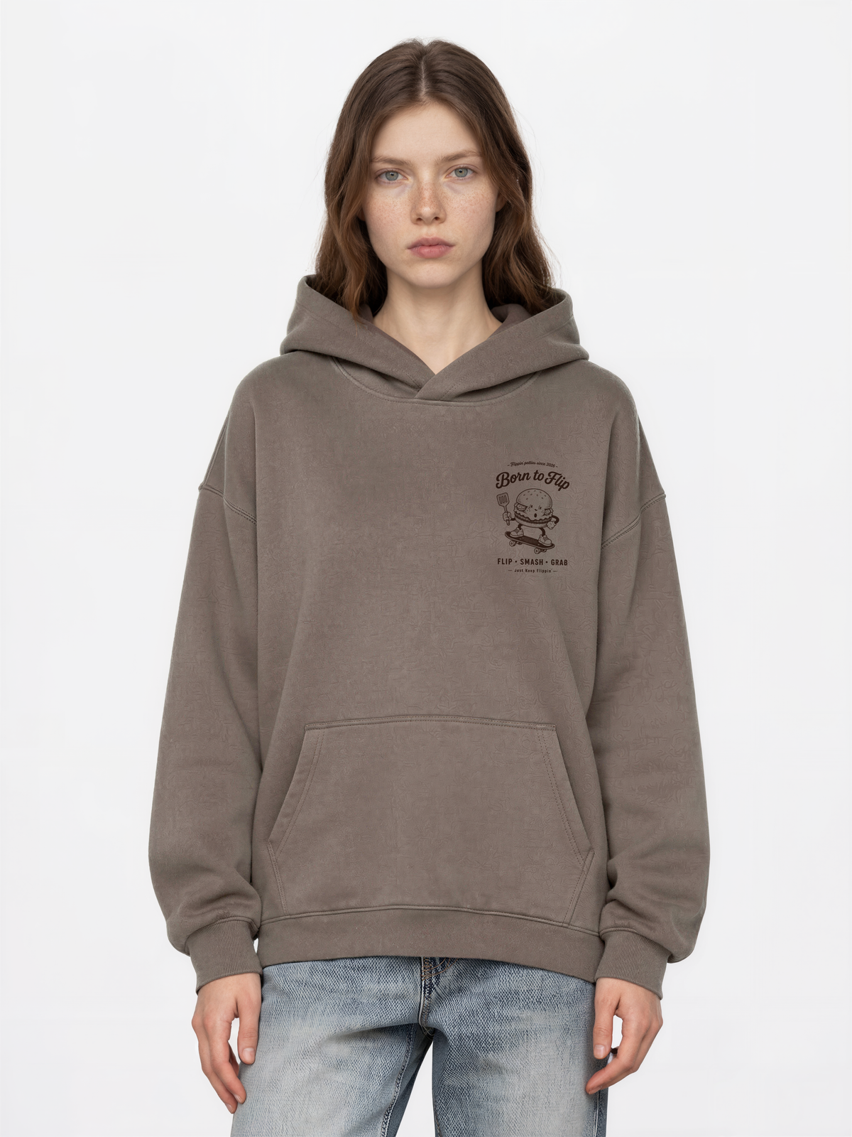 Female model wearing the Born to Flip taupe oversized hoodie, front view with small brown burger artwork on the left chest.