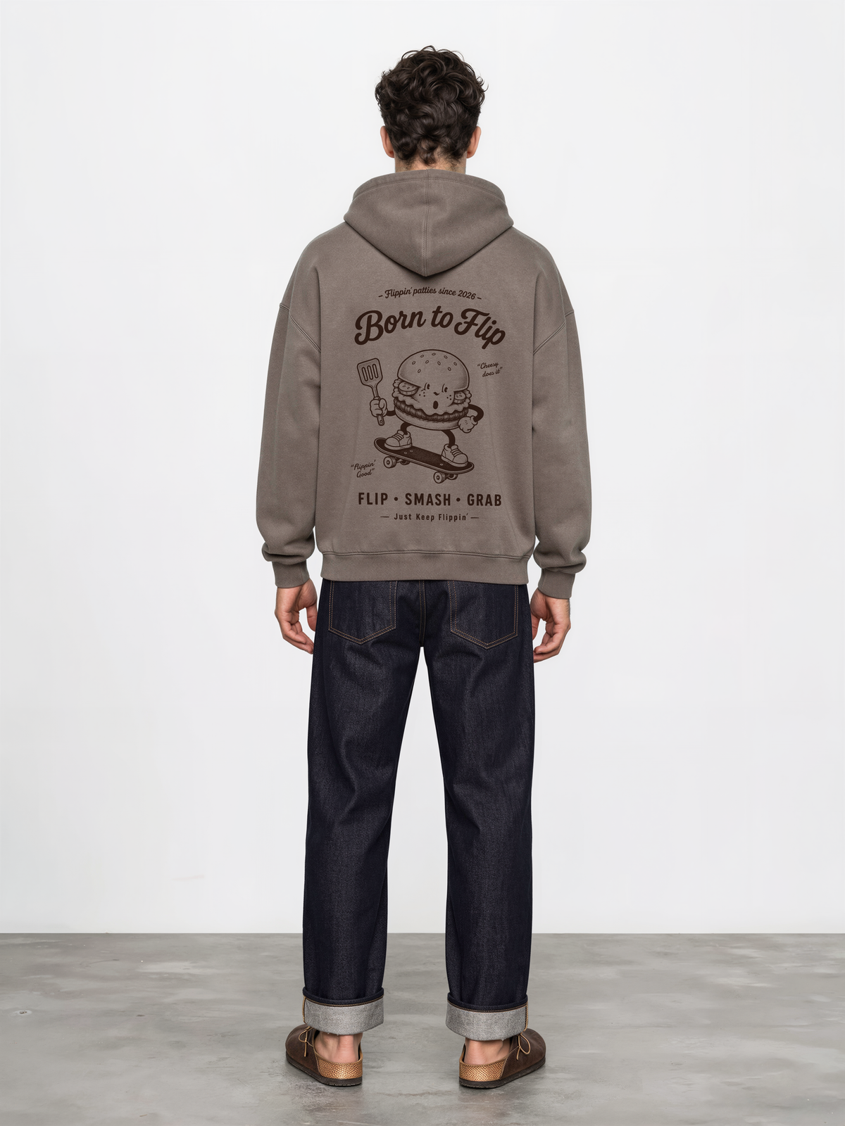 Male model wearing the Born to Flip taupe oversized hoodie, back view with large brown skateboarding burger artwork across the back.