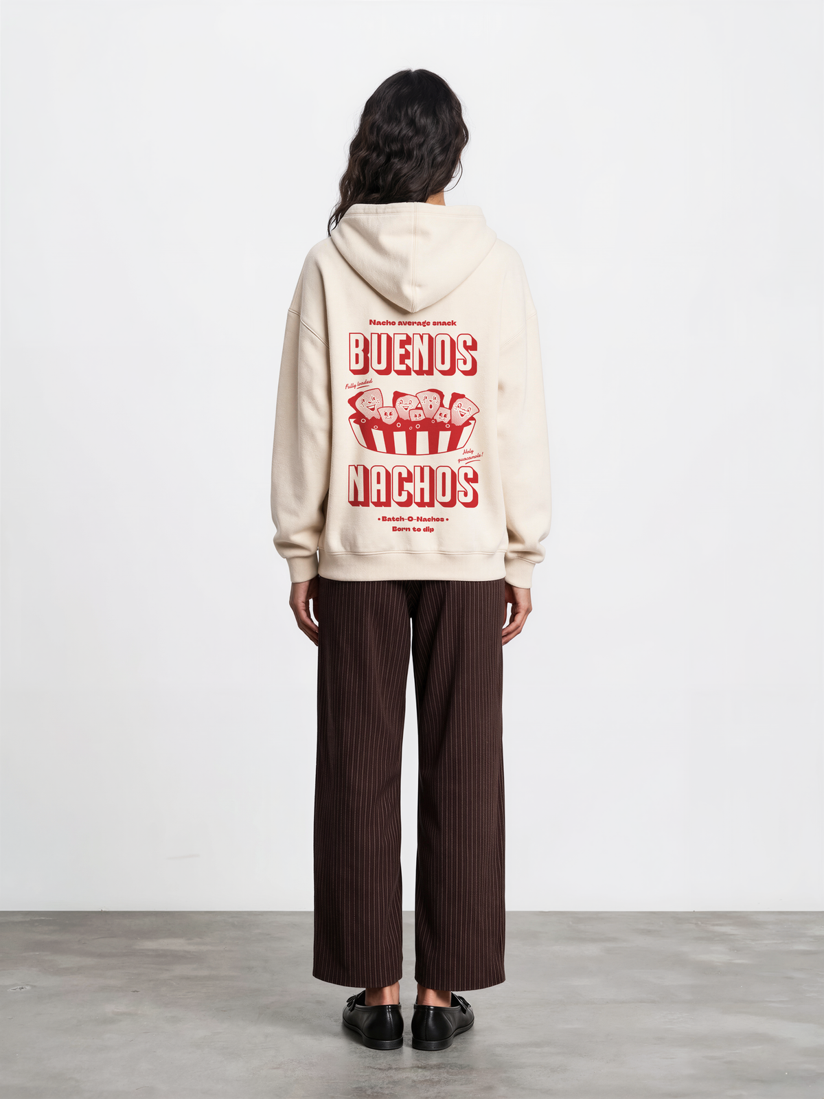Female model wearing the Buenos Nachos ivory oversized hoodie, back view showing the red nacho illustration and lettering on the back.