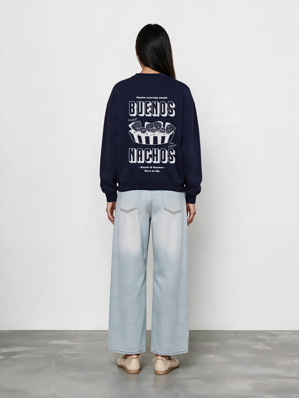 Female model wearing the Buenos Nachos navy oversized sweatshirt, back view showing the white nacho illustration and lettering on the back.
