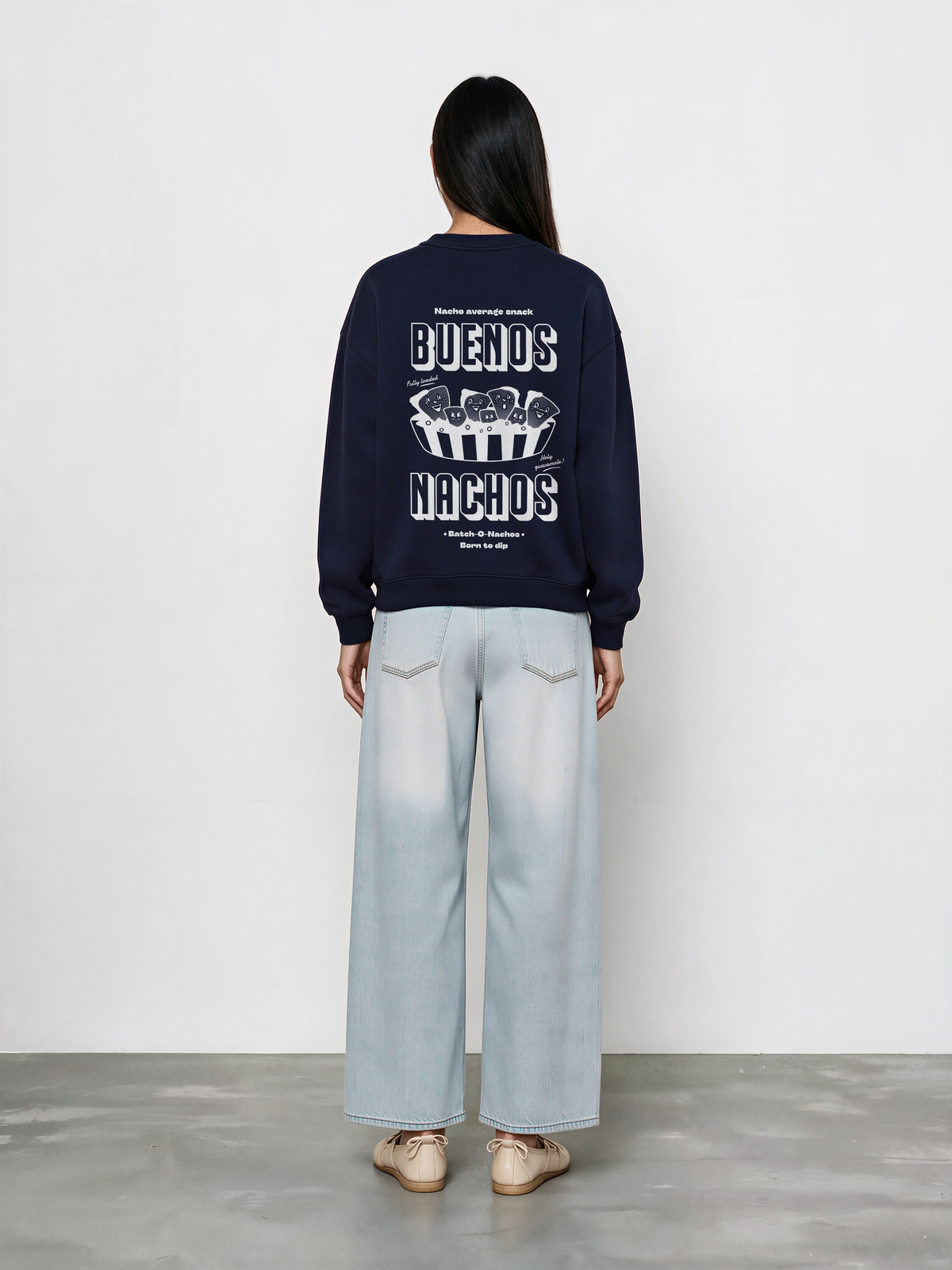 Female model wearing the Buenos Nachos navy oversized sweatshirt, back view showing the white nacho illustration and lettering on the back.