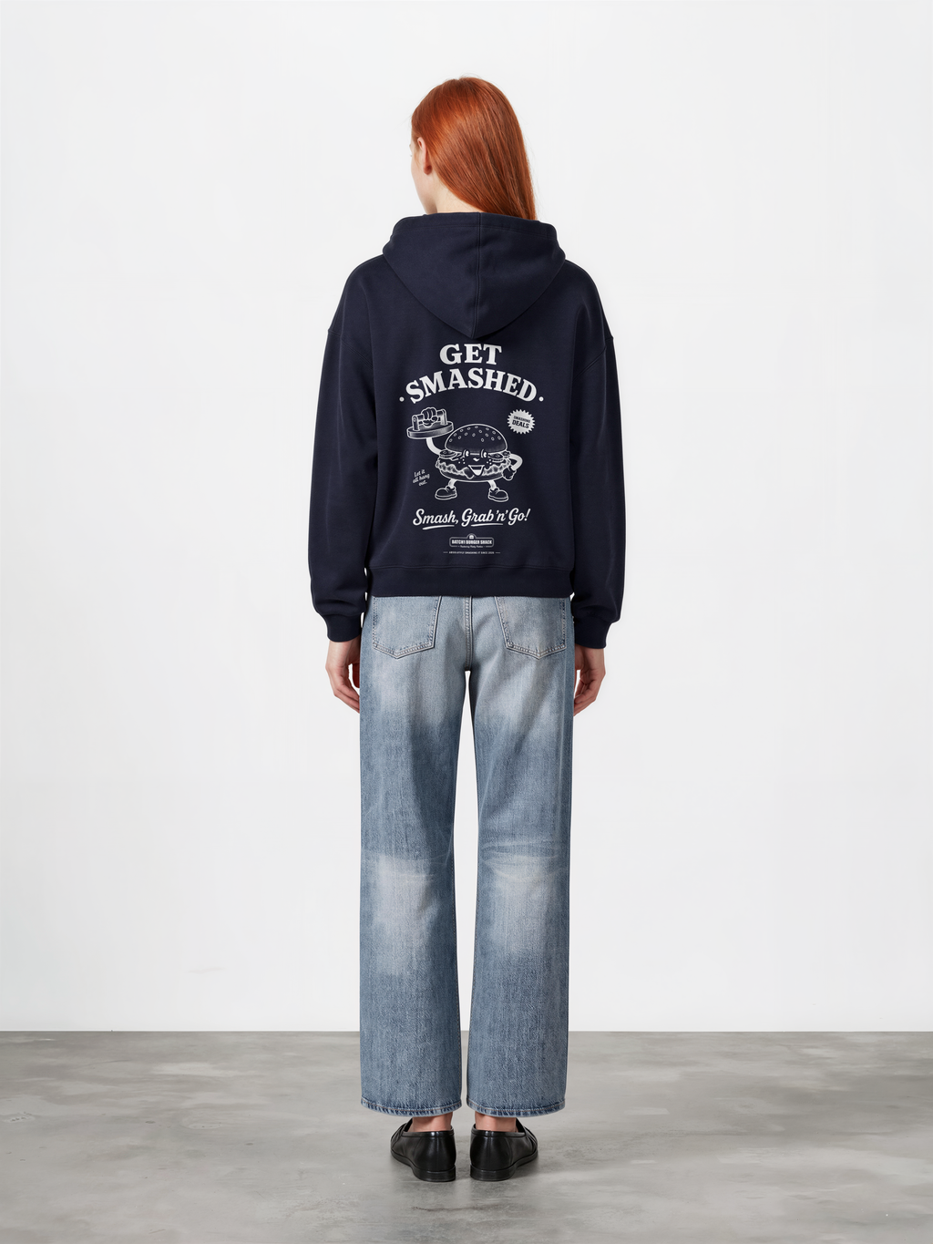 Female model wearing the Get Smashed navy oversized hoodie, back view showing the large white burger character and Get Smashed lettering beneath the hood.