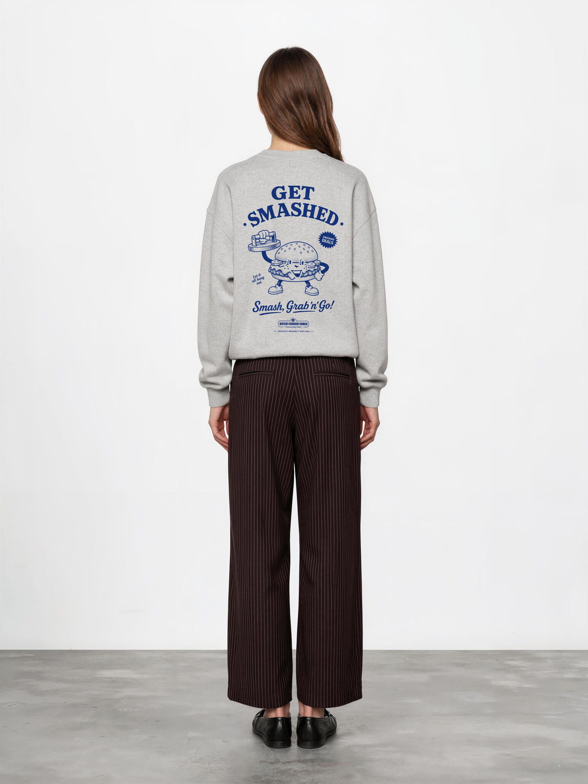 Female model wearing the Get Smashed ash oversized sweatshirt, back view showing the large blue burger character and Get Smashed lettering on the back.