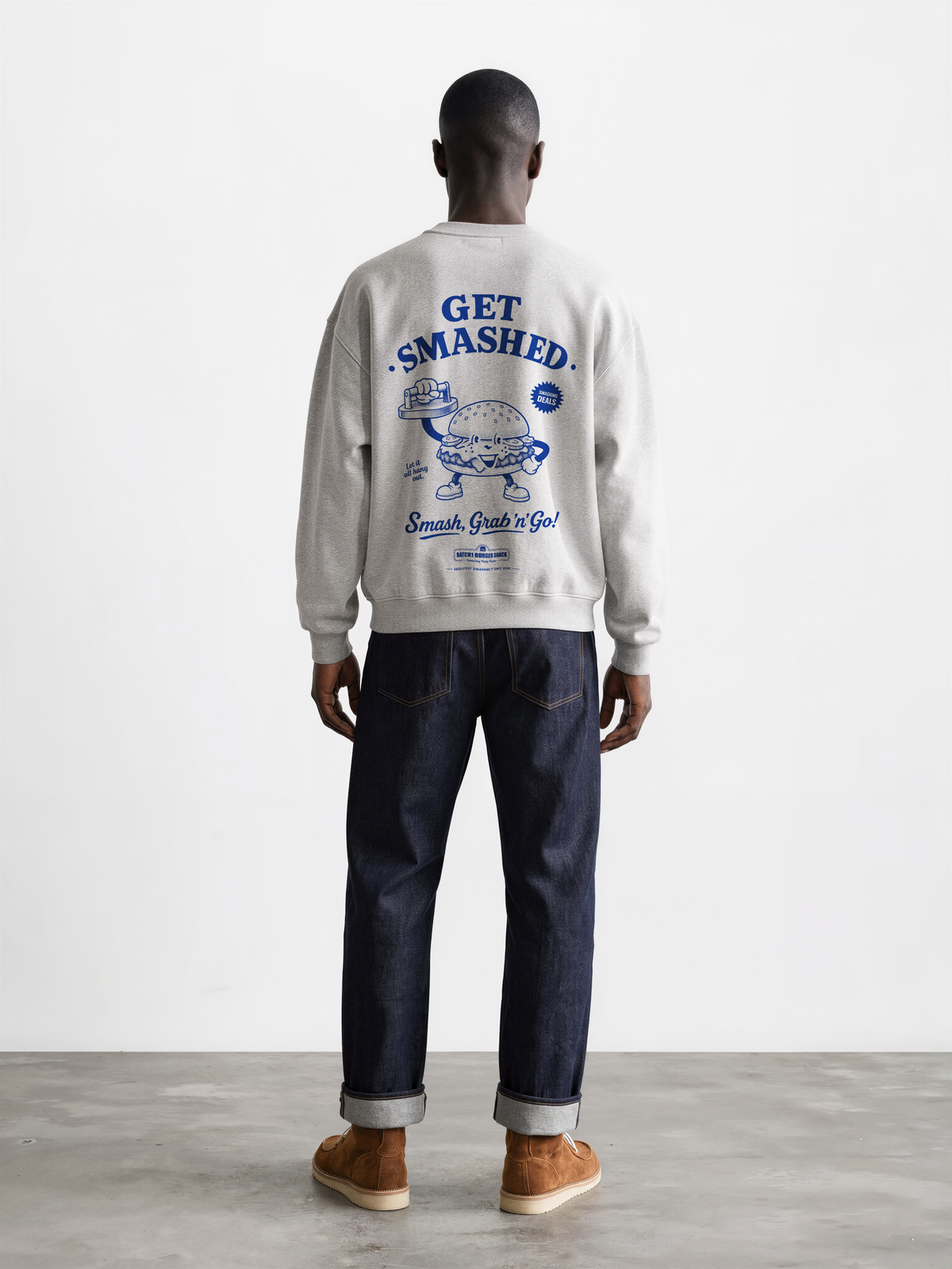 Male model wearing the Get Smashed ash oversized sweatshirt, back view showing the large blue burger character and Get Smashed lettering on the back.