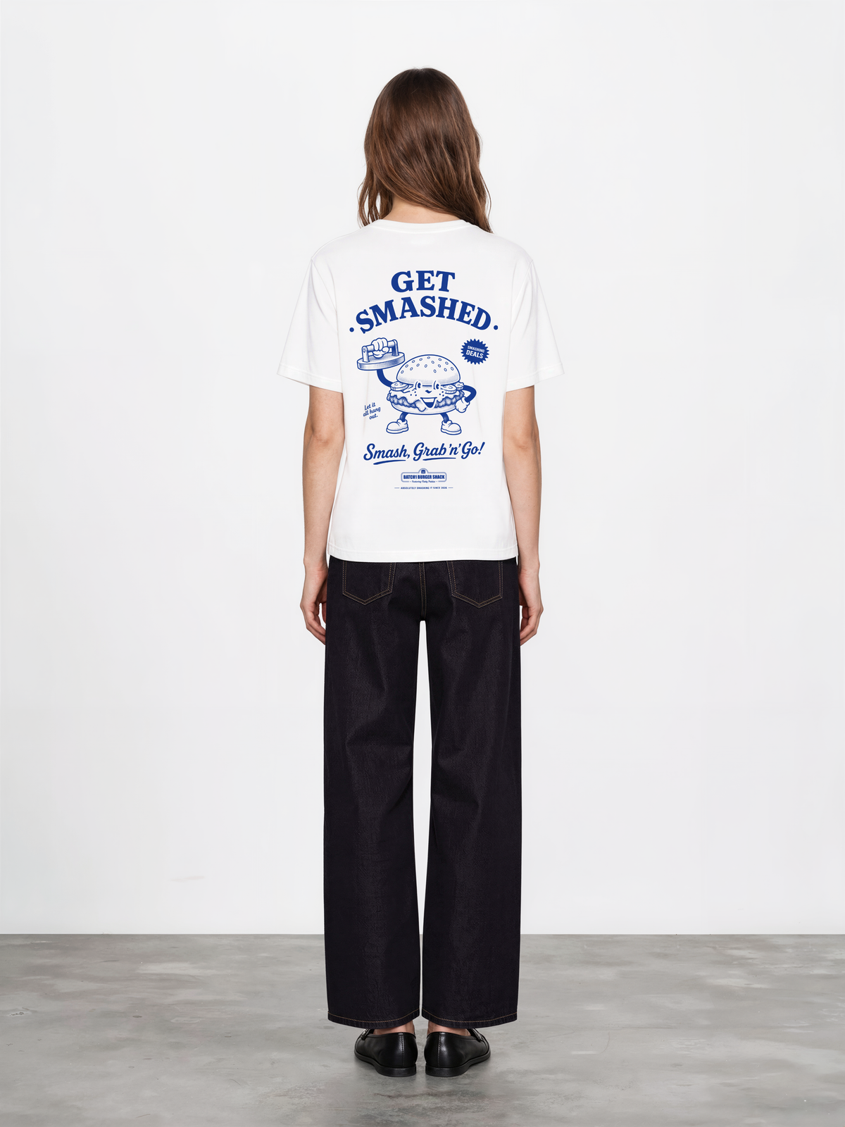 Female model wearing the Get Smashed white T-shirt, back view showing the large blue burger character and Get Smashed lettering on the back.