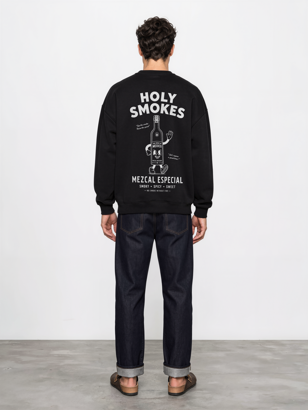 Male model wearing the black Holy Smokes oversized sweatshirt, showing the large white Holy Smokes mezcal bottle screen print on the back