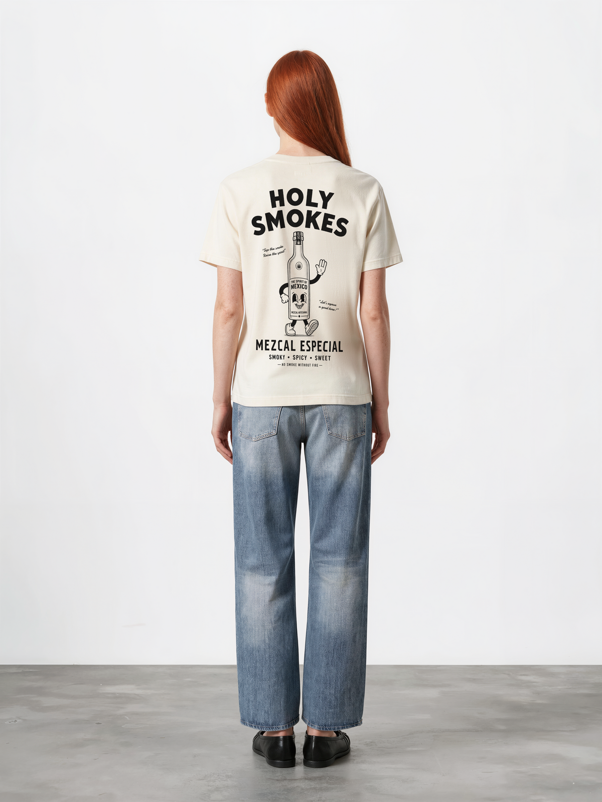 Female model wearing the ivory Holy Smokes T-shirt, showing the large black Holy Smokes mezcal bottle artwork on the back
