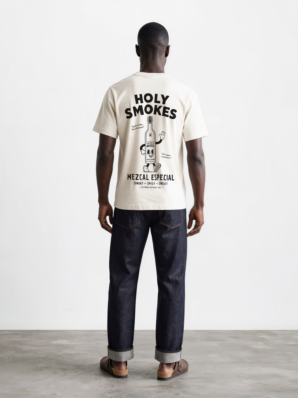 Male model wearing the ivory Holy Smokes T-shirt, showing the large black Holy Smokes mezcal bottle artwork on the back