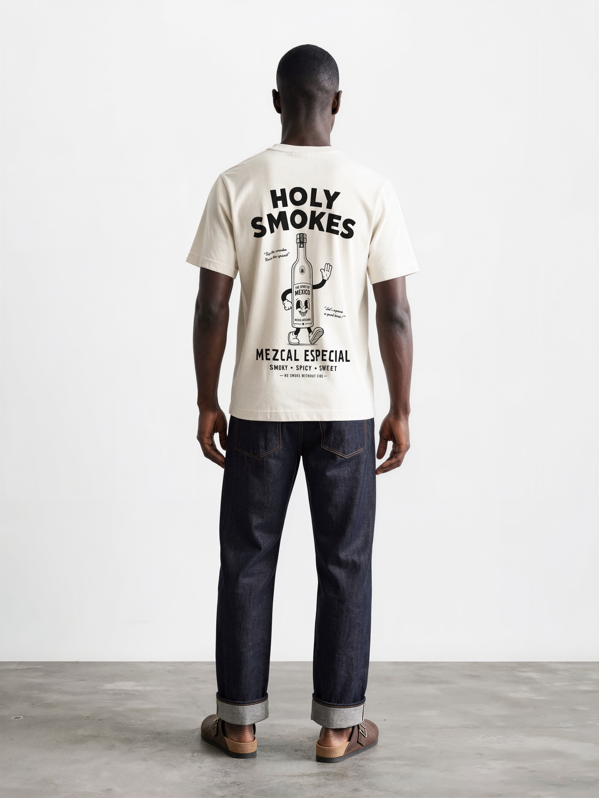 Male model wearing the ivory Holy Smokes T-shirt, showing the large black Holy Smokes mezcal bottle artwork on the back