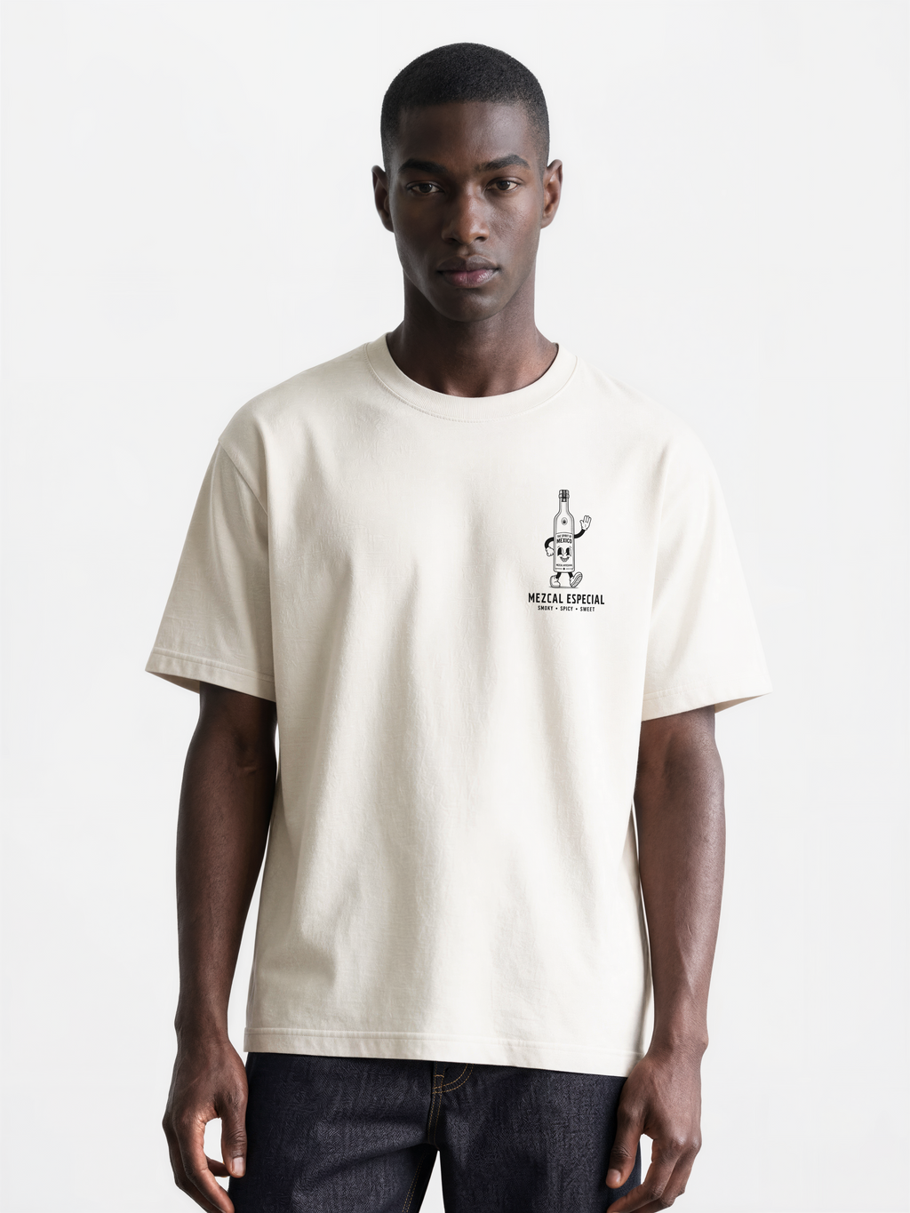 Male model wearing the ivory Holy Smokes T-shirt, showing the small black mezcal bottle print on the left chest