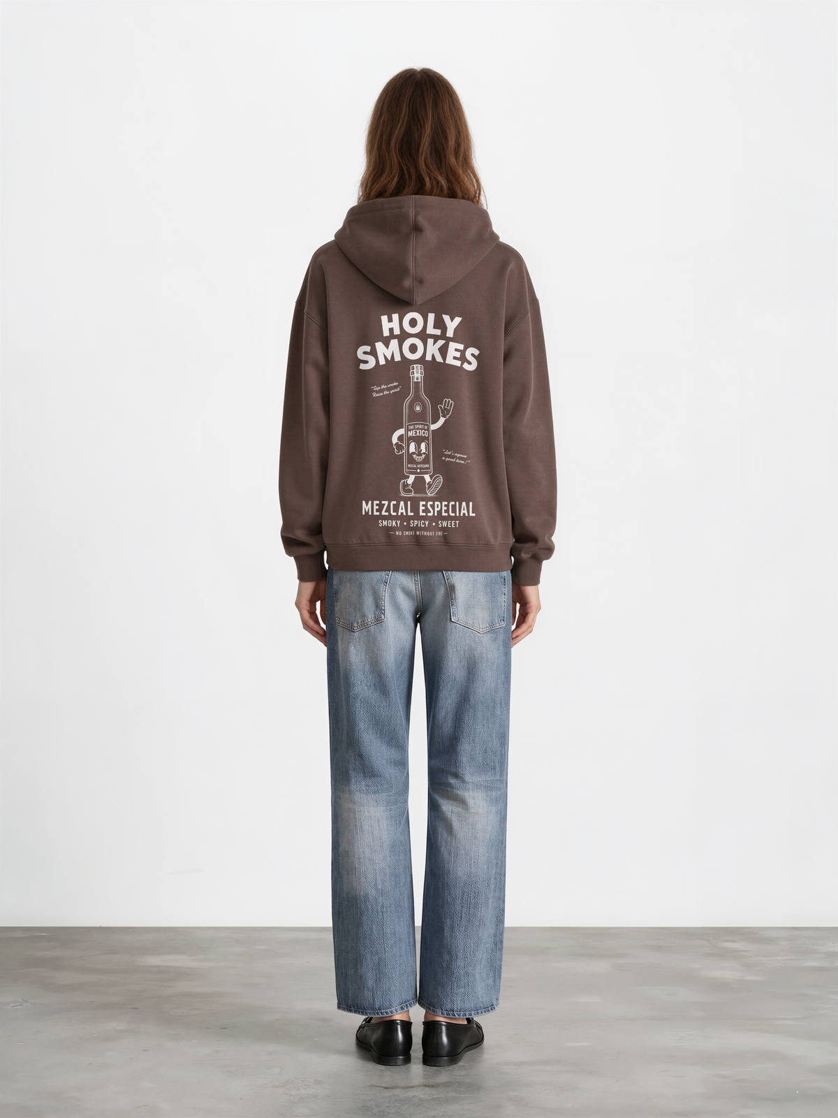 Female model wearing the mocha Holy Smokes oversized hoodie, showing the large white Holy Smokes mezcal bottle screen print on the back