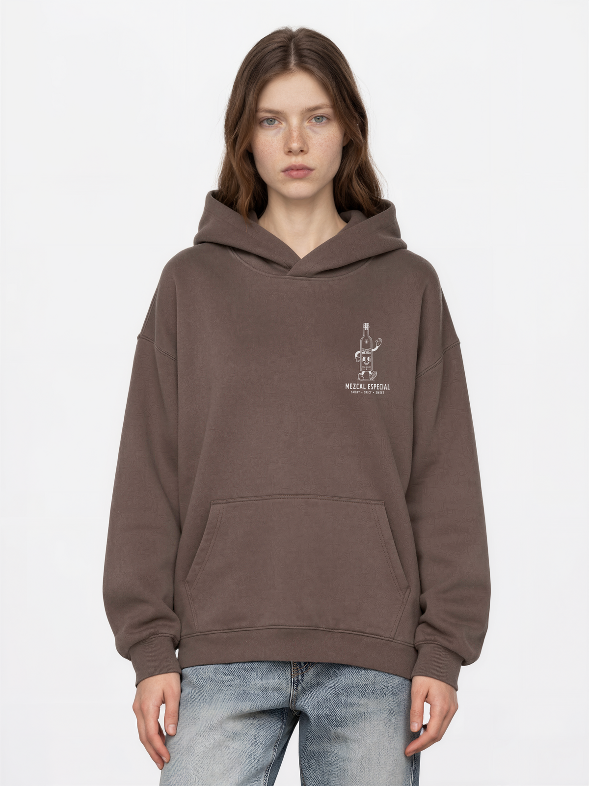 Female model wearing the mocha Holy Smokes oversized hoodie, showing the small white mezcal bottle screen print on the left chest