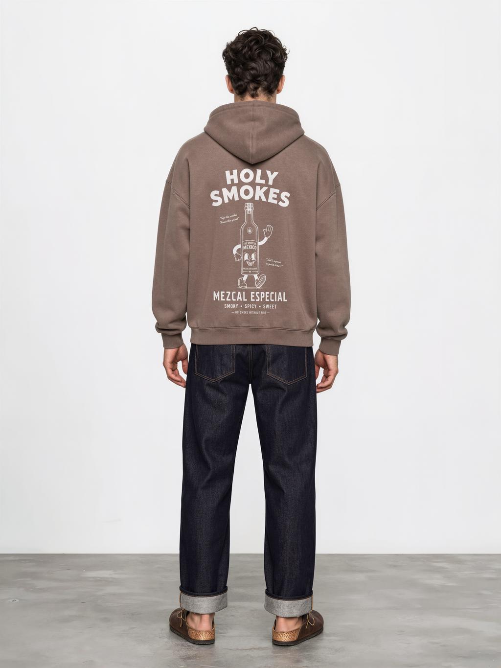 Male model wearing the mocha Holy Smokes oversized hoodie, showing the large white Holy Smokes mezcal bottle screen print on the back