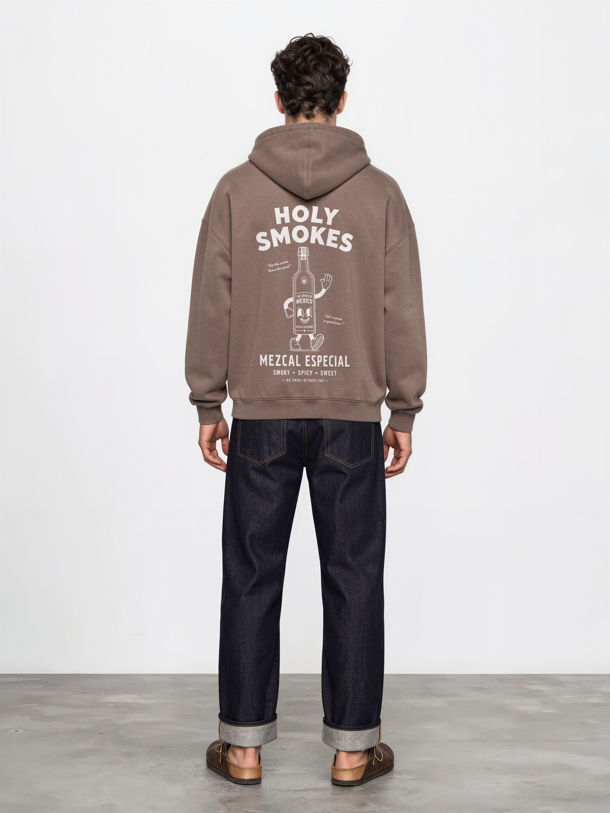 Male model wearing the mocha Holy Smokes oversized hoodie, showing the large white Holy Smokes mezcal bottle screen print on the back