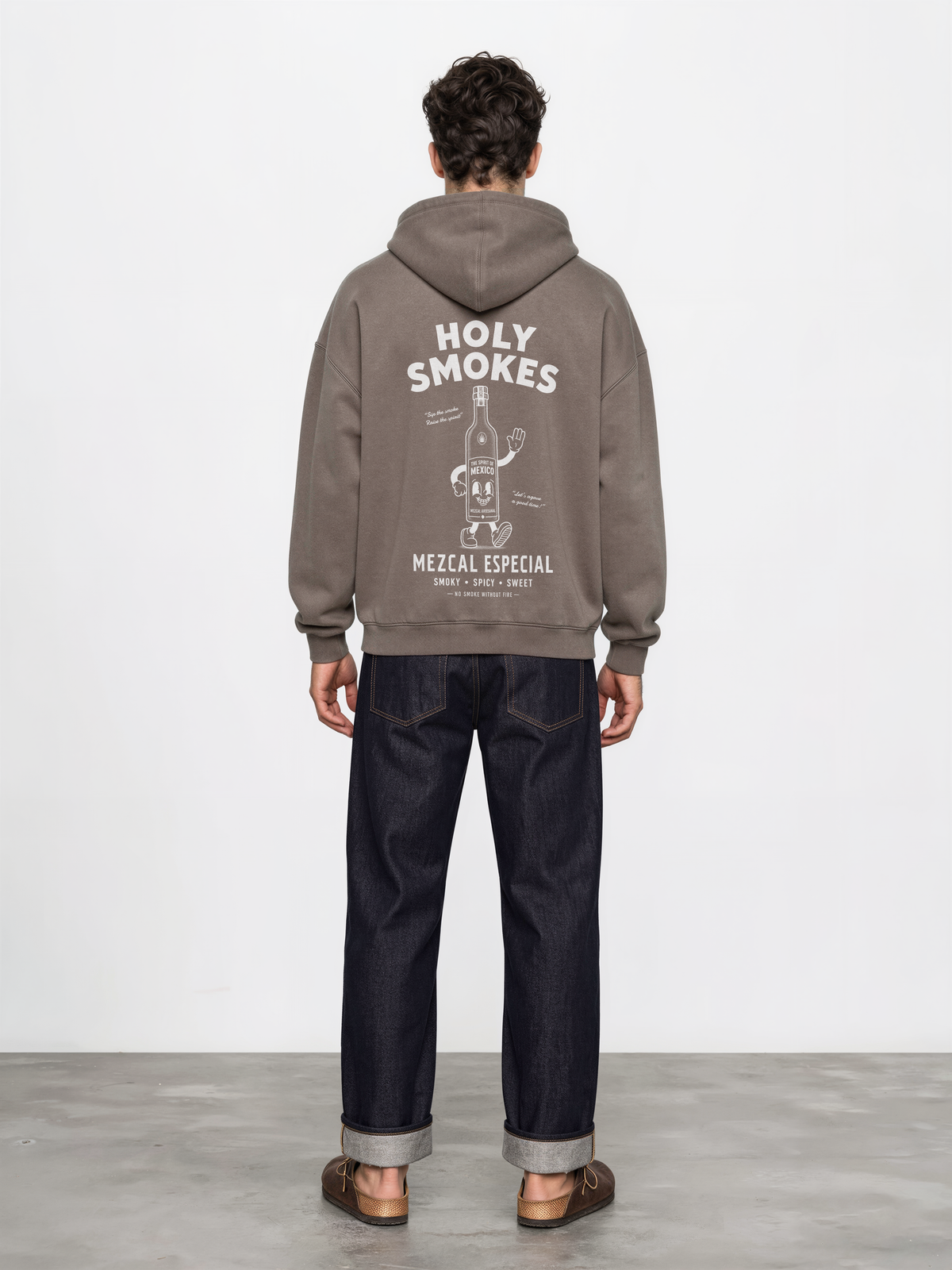 Male model wearing the taupe Holy Smokes oversized hoodie, showing the large white Holy Smokes mezcal bottle screen print on the back