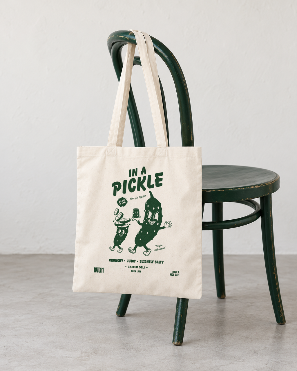 In a Pickle natural cotton tote bag with green pickle print hanging from a bottle-green bistro chair