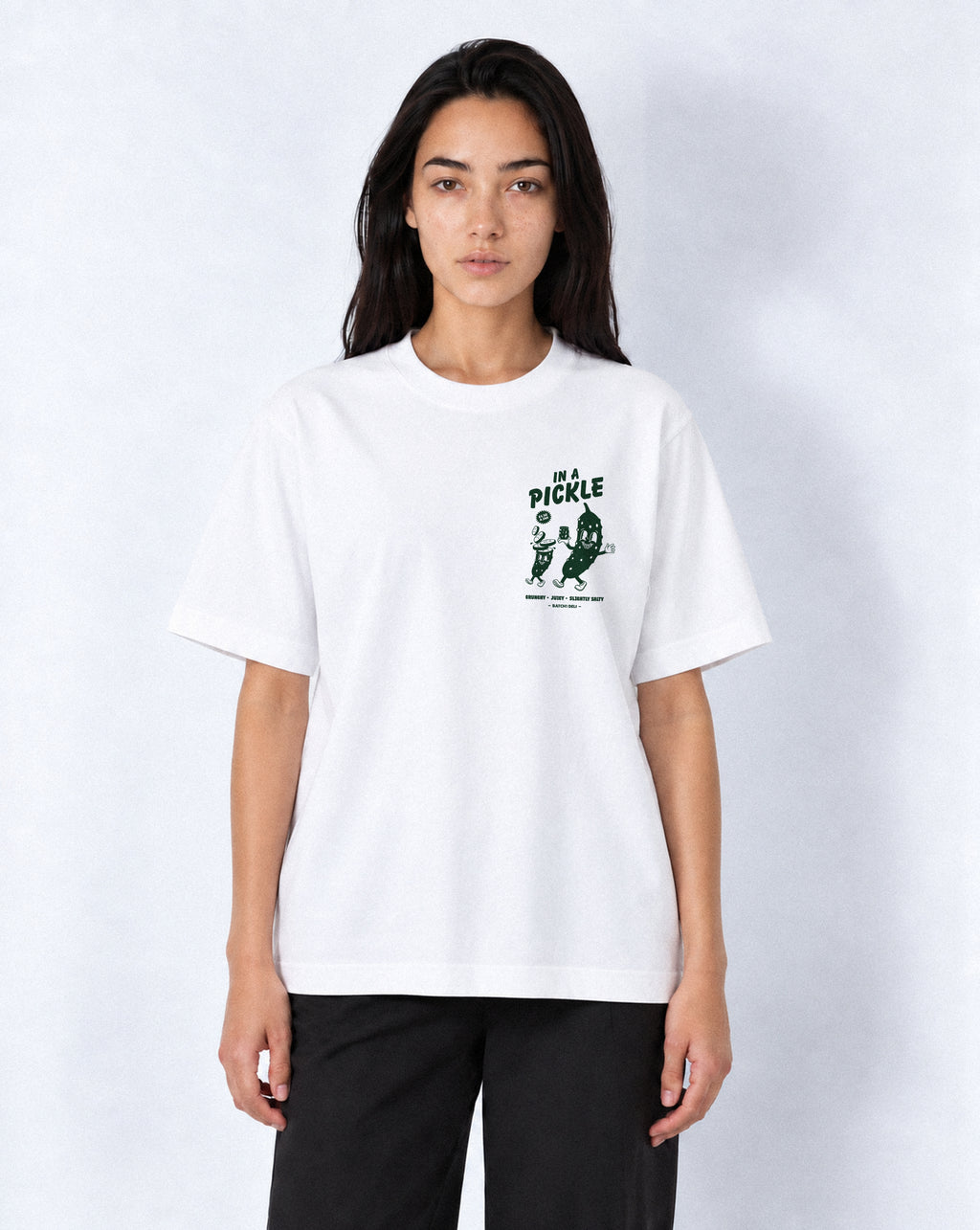 Female model wearing the Batch1 In a Pickle white T-shirt, front view with dark green left-chest print.