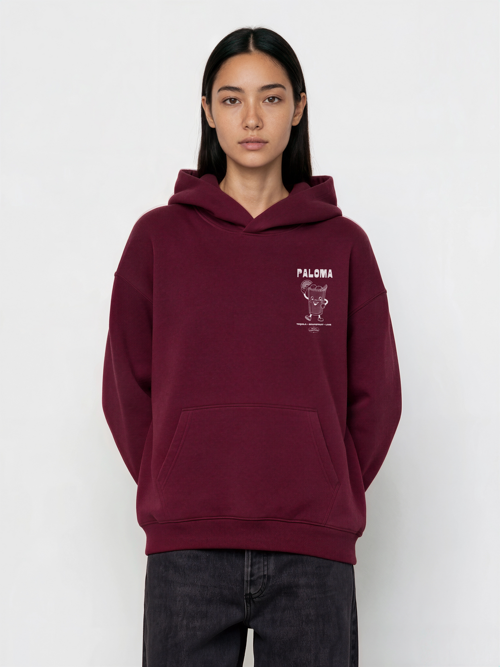 Female model wearing the Paloma burgundy oversized hoodie, front view showing the smaller white left-chest cocktail print.