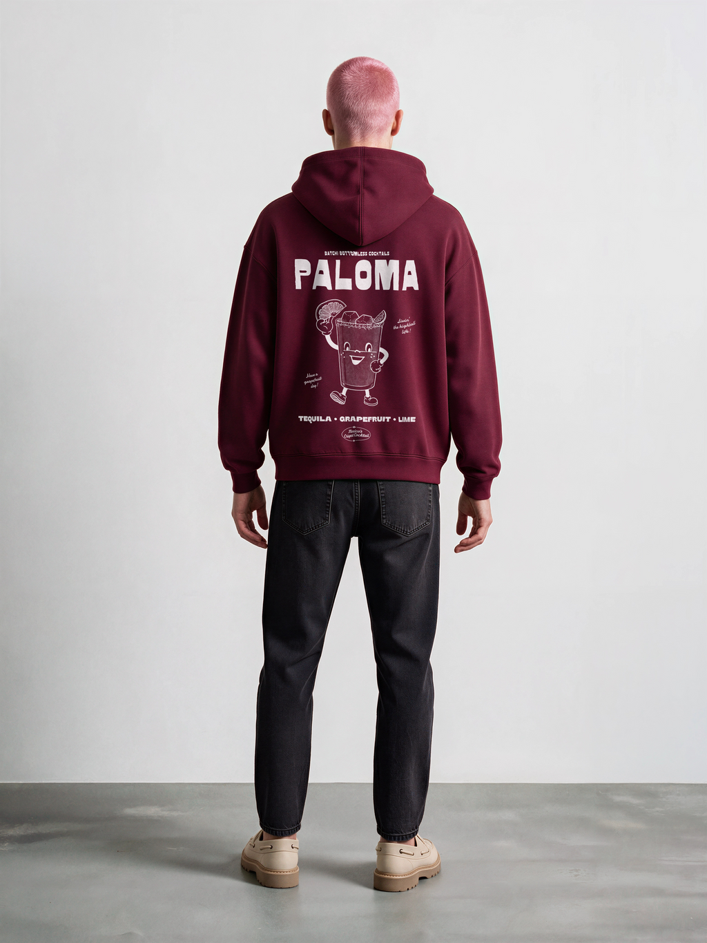 Male model wearing the Paloma burgundy oversized hoodie, back view showing the white cocktail graphic just beneath the hood.