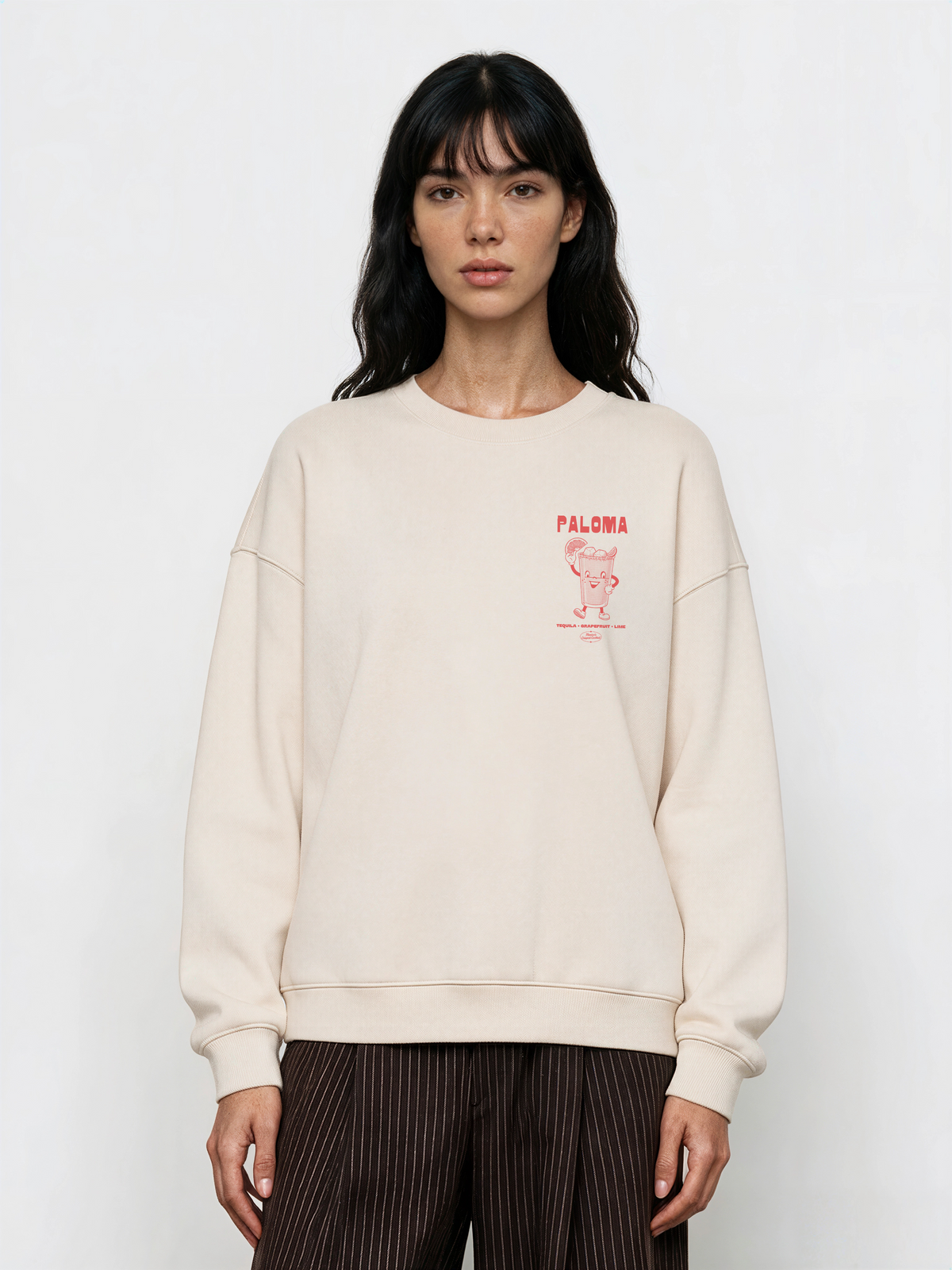 Female model wearing the Paloma ivory oversized sweatshirt, front view showing the coral cocktail graphic on the left chest.