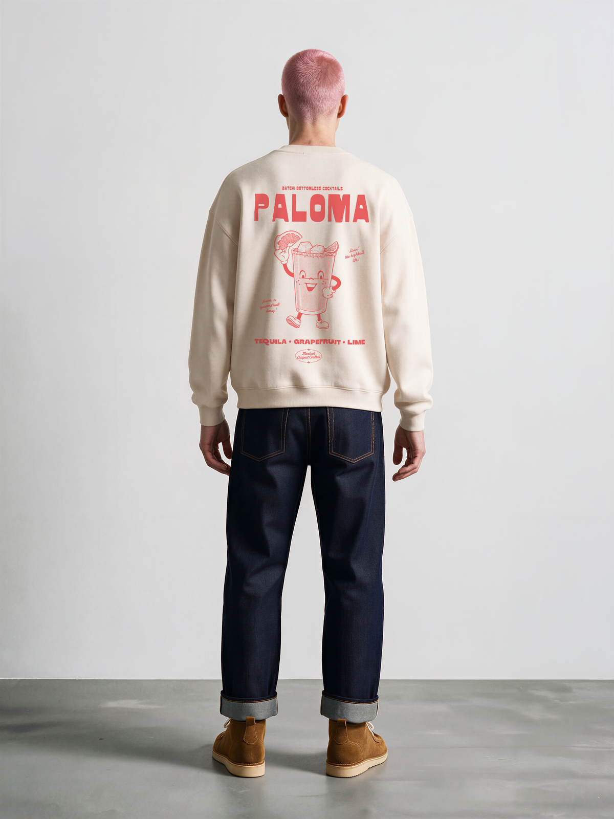 Male model wearing the Paloma ivory oversized sweatshirt, back view showing the large coral Paloma cocktail graphic following the fabric folds.