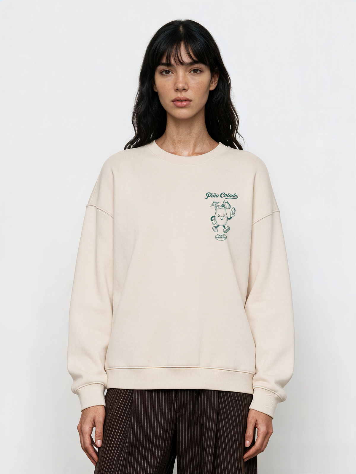 Female model wearing the Piña Colada ivory oversized sweatshirt, showing the small teal Piña Colada cocktail print on the left chest.