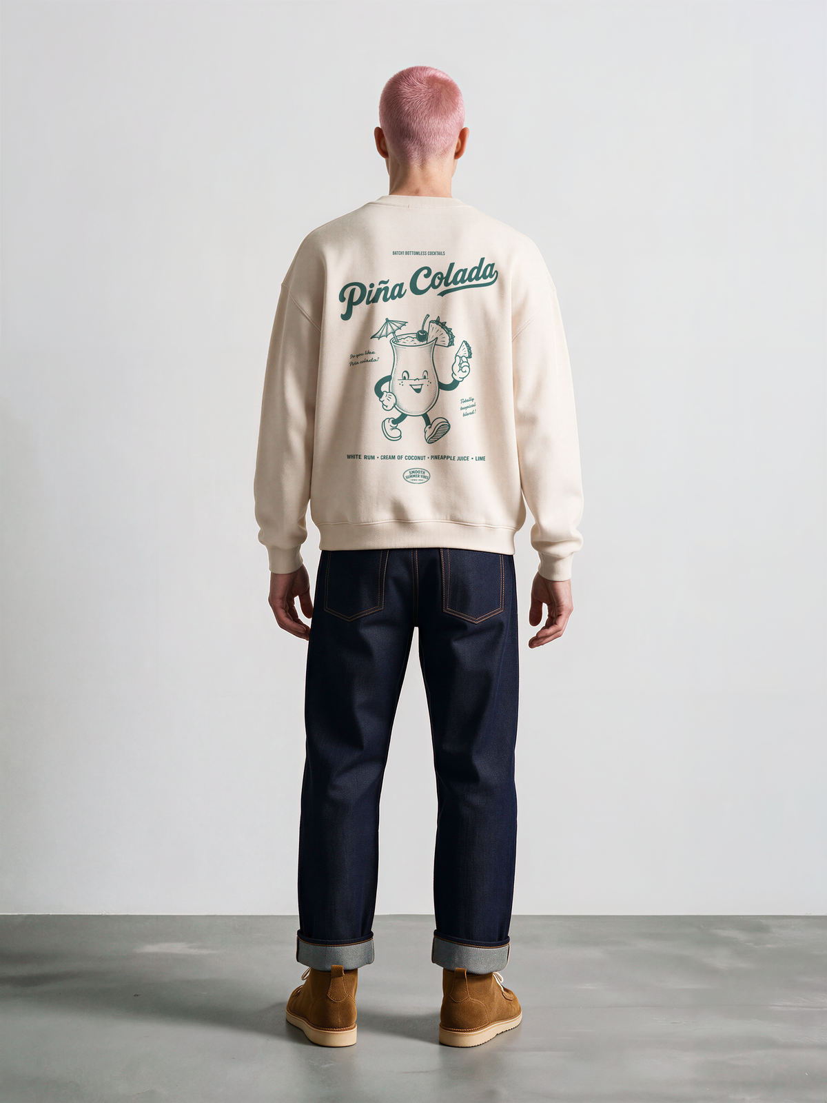 Male model wearing the Piña Colada ivory oversized sweatshirt, showing the large teal tropical cocktail character and Piña Colada lettering on the back.