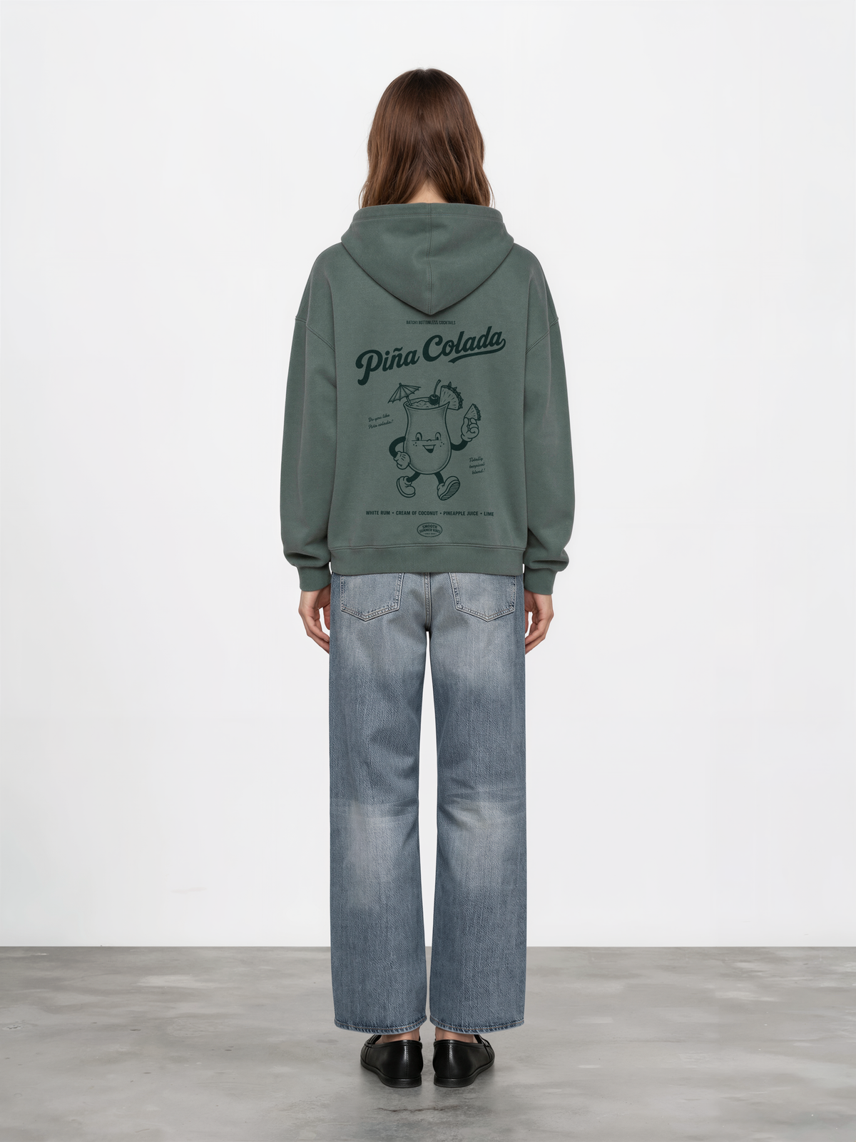 Female model wearing the Piña Colada pine oversized hoodie, showing the large teal tropical cocktail character and Piña Colada lettering on the back.