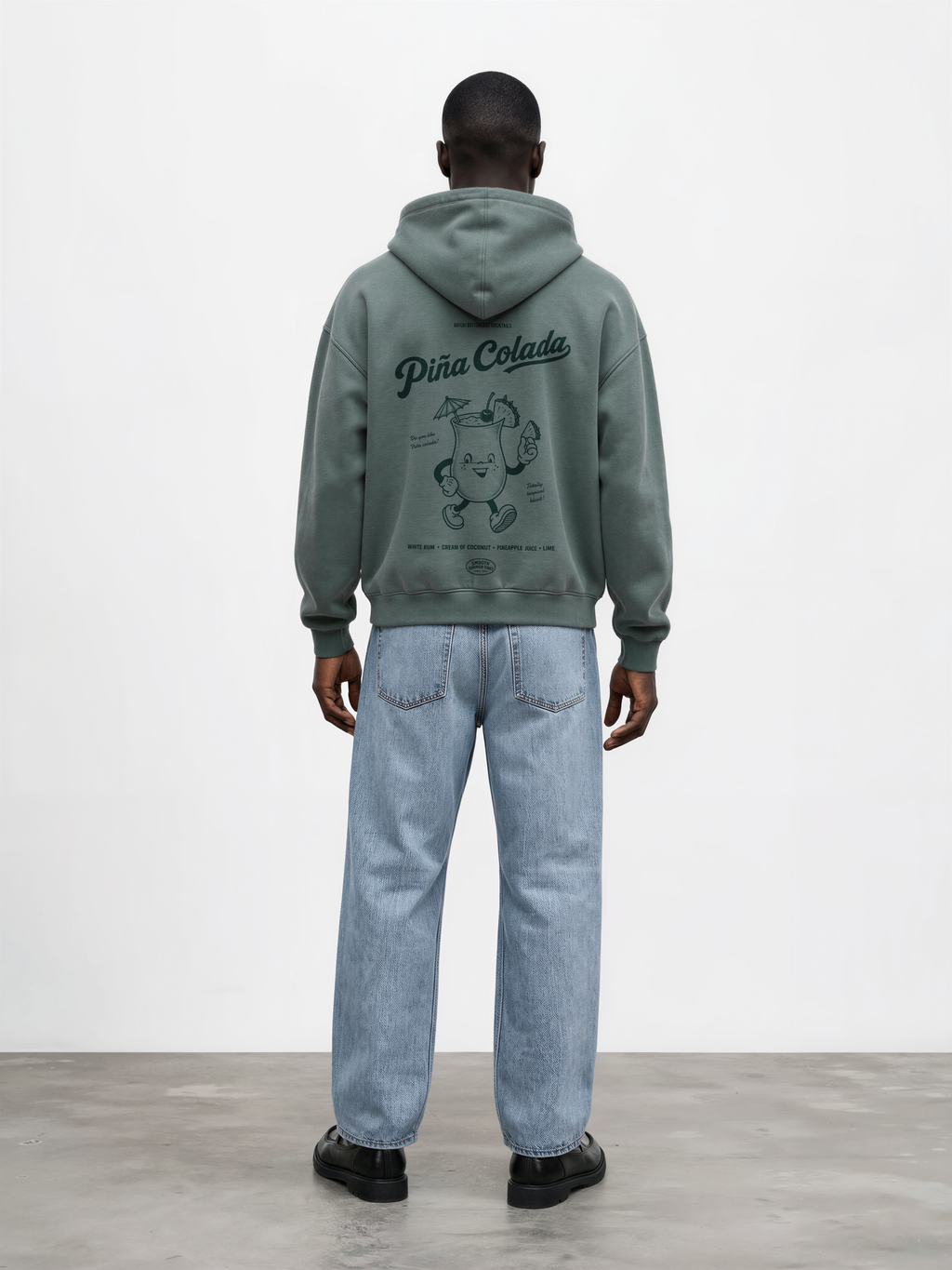 Male model wearing the Piña Colada pine oversized hoodie, showing the large teal tropical cocktail character and Piña Colada lettering on the back.