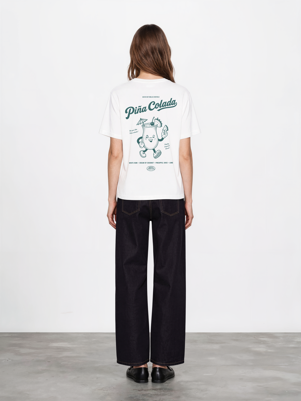 Female model wearing the Piña Colada white T-shirt, back view showing the large teal tropical cocktail graphic.