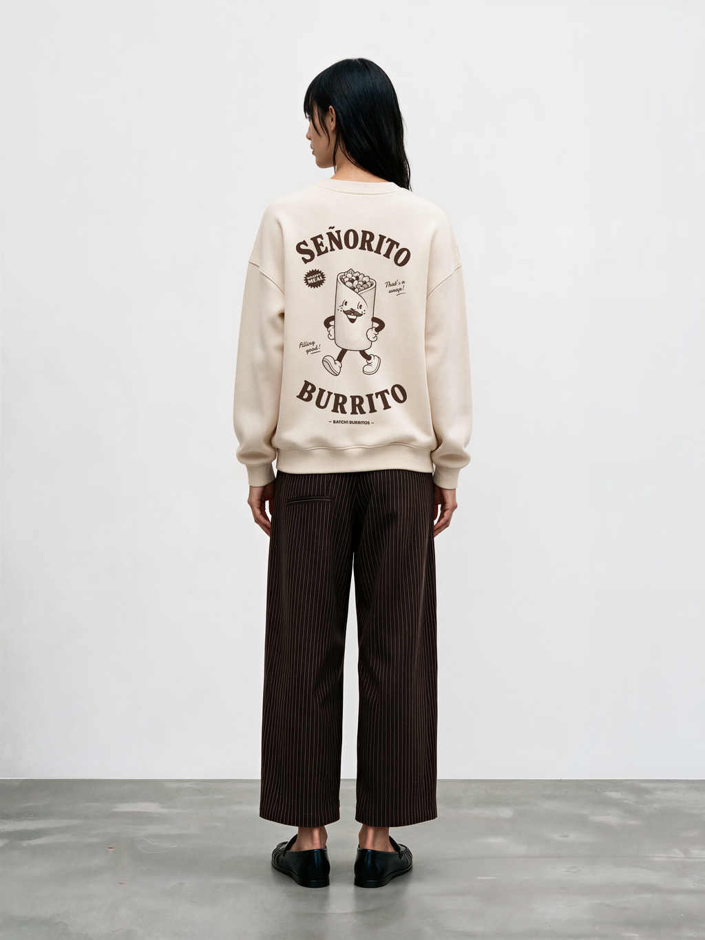 Female model wearing the Señorito Burrito ivory oversized sweatshirt, back view showing the dark brown large burrito character and lettering.