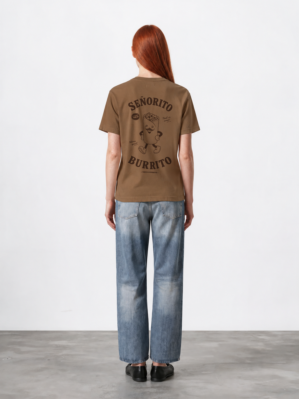 Female model wearing the Señorito Burrito tobacco T-shirt, back view showing the large dark brown burrito character and lettering.