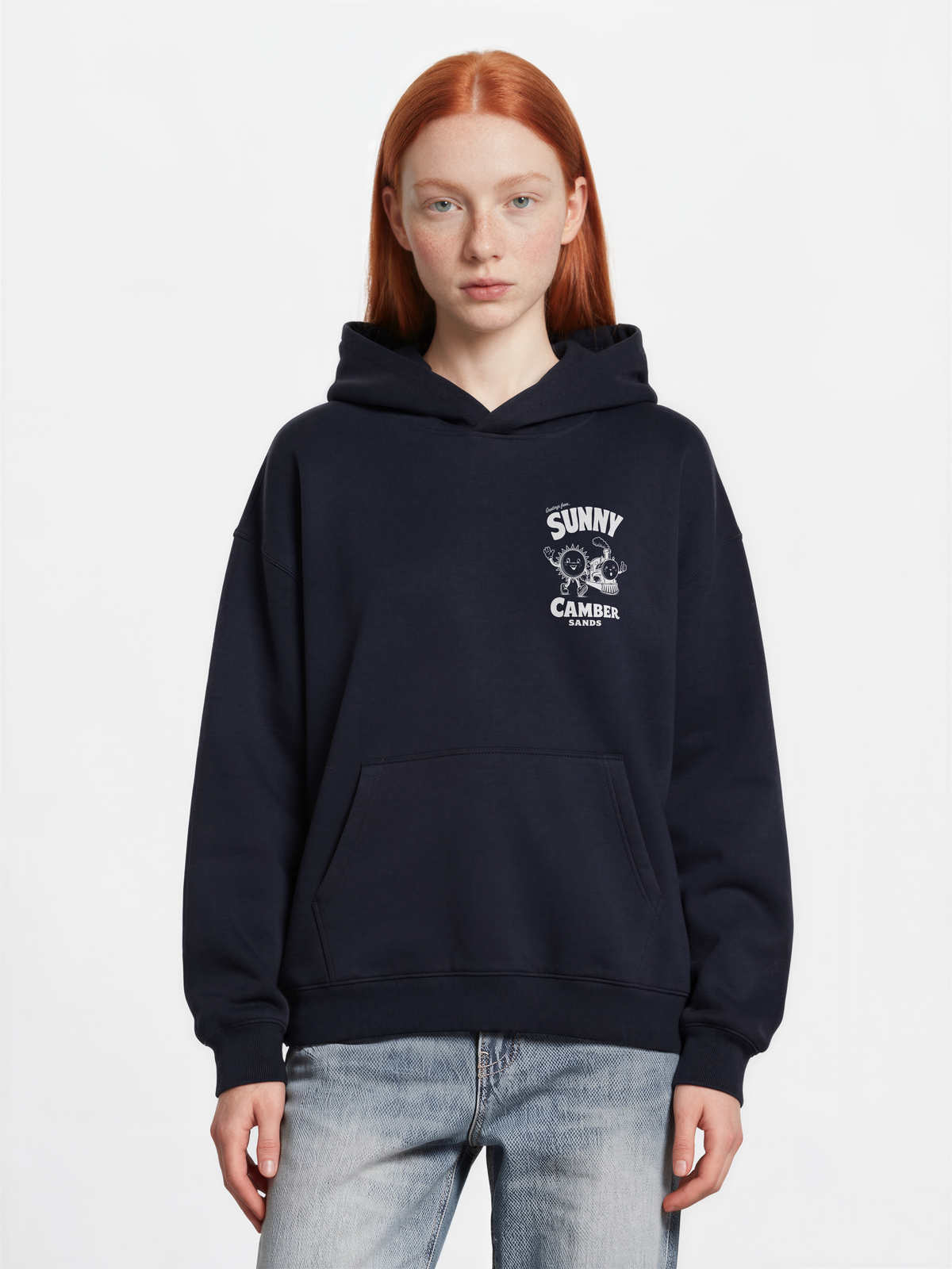 Sunny Camber Sands navy hoodie, front female model view, showing a small white sun and steam train chest print